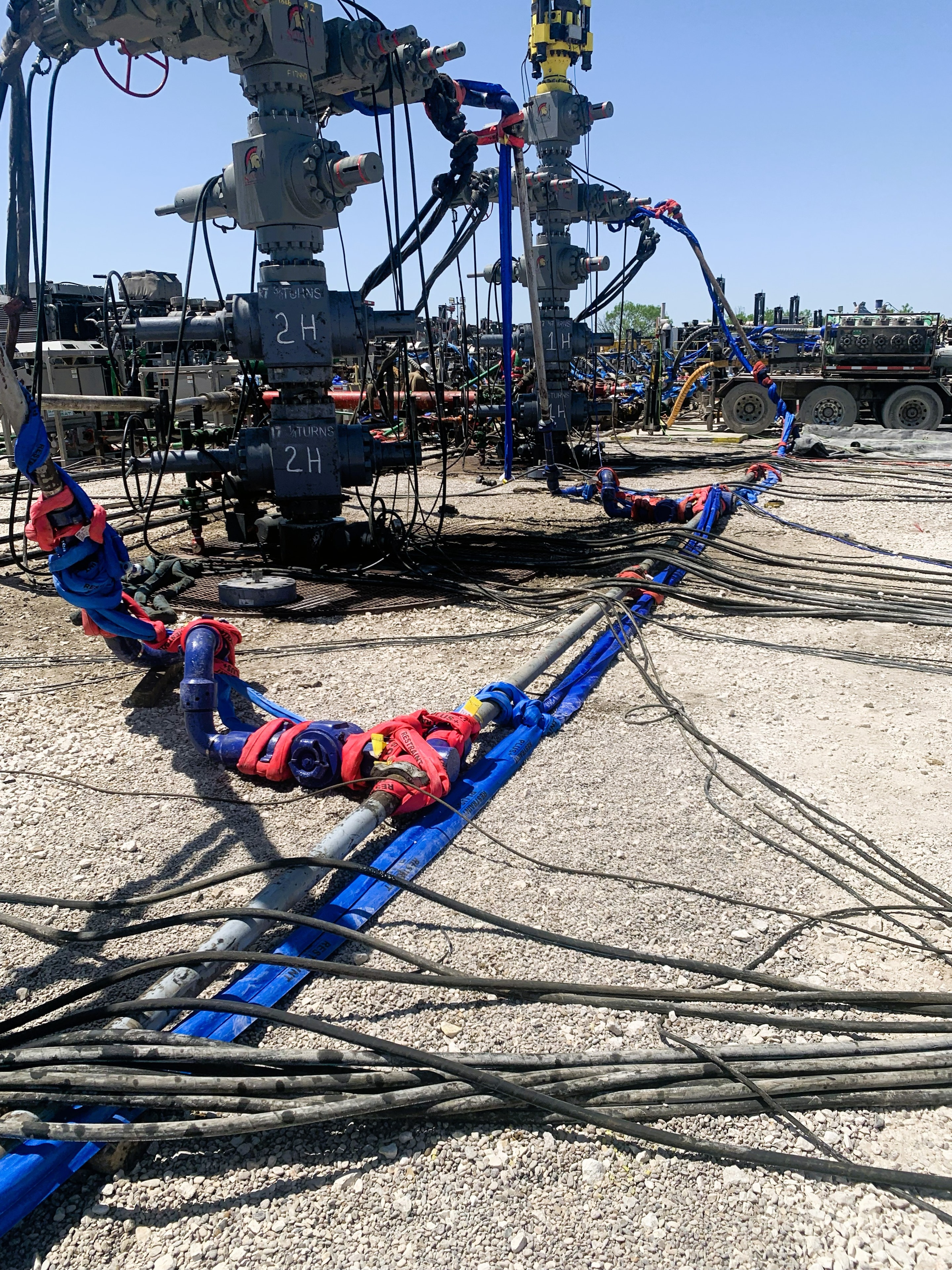 SureHold blue restraint straps on wellheads and flowlines across a wide active frac site